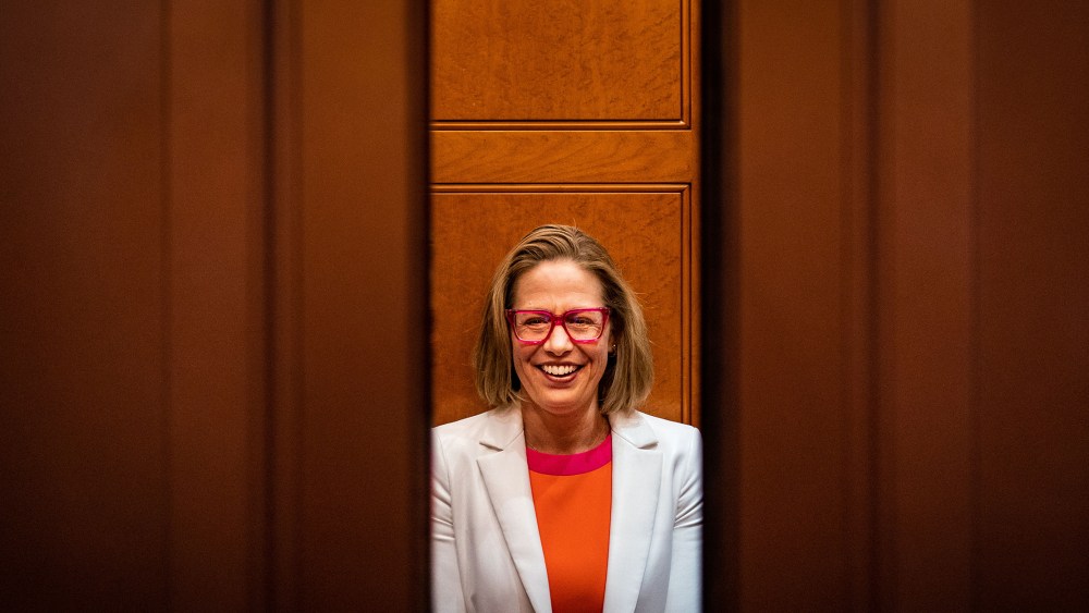 Image: Sen. Kyrsten Sinema (D-AZ) smiling while talking to reporters as the elevator door closes.