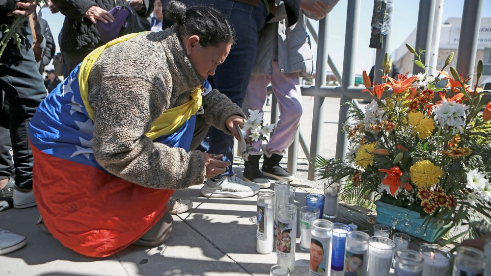 A woman places flowers in front of a gate that has been converted into a memorial outside a Mexican immigration detention center