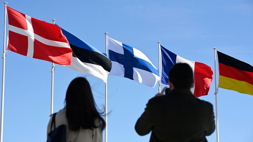 People stand in front of the Finnish national flag, center, after a flag-raising ceremony at the NATO headquarters in Brussels