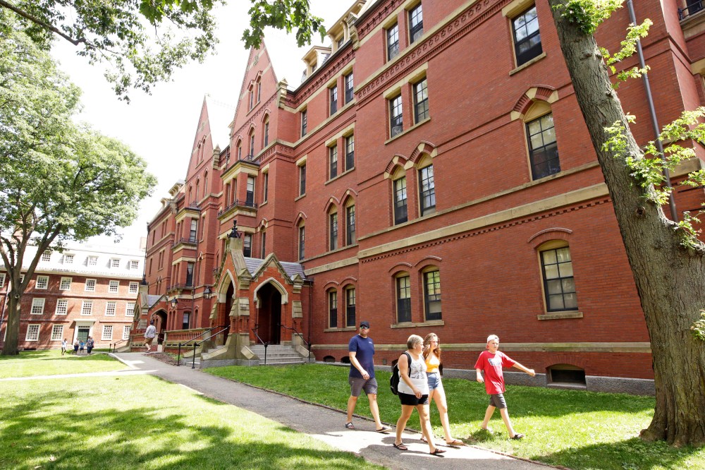 People walk along a sidewalk on the campus of Harvard University