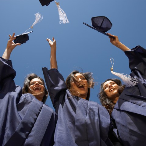 Three female graduate students throwing mortar boards, low angle view