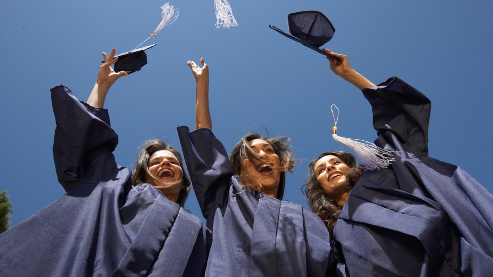 Three female graduate students throwing mortar boards, low angle view