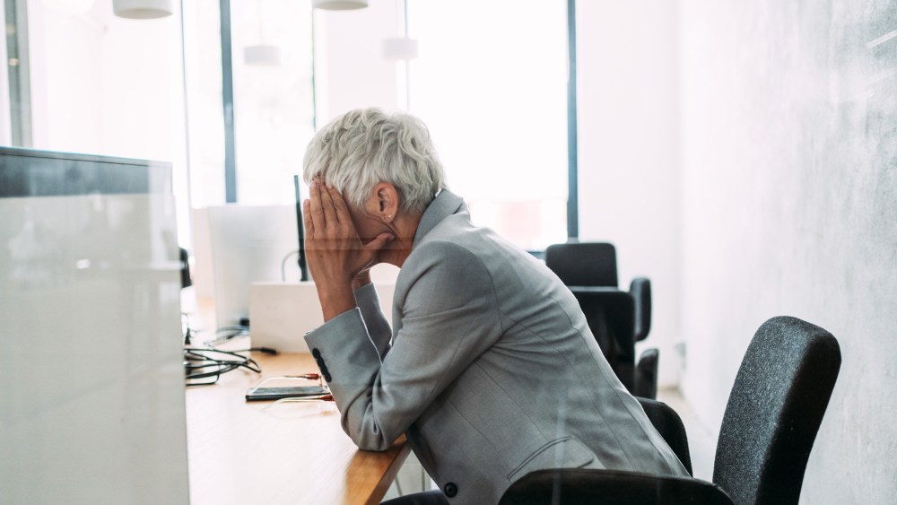 A woman holds her head in her hands at a desk.