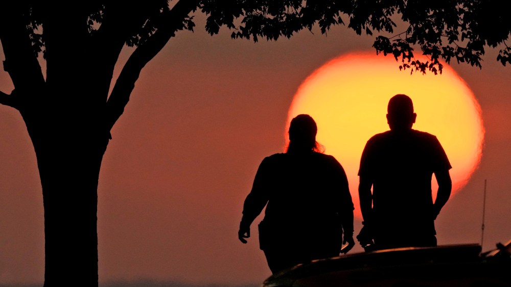 A couple watches the sunset as triple-digit heat indexes continue in the Midwest Sunday, Aug. 20, 2023, in Kansas City, Mo.