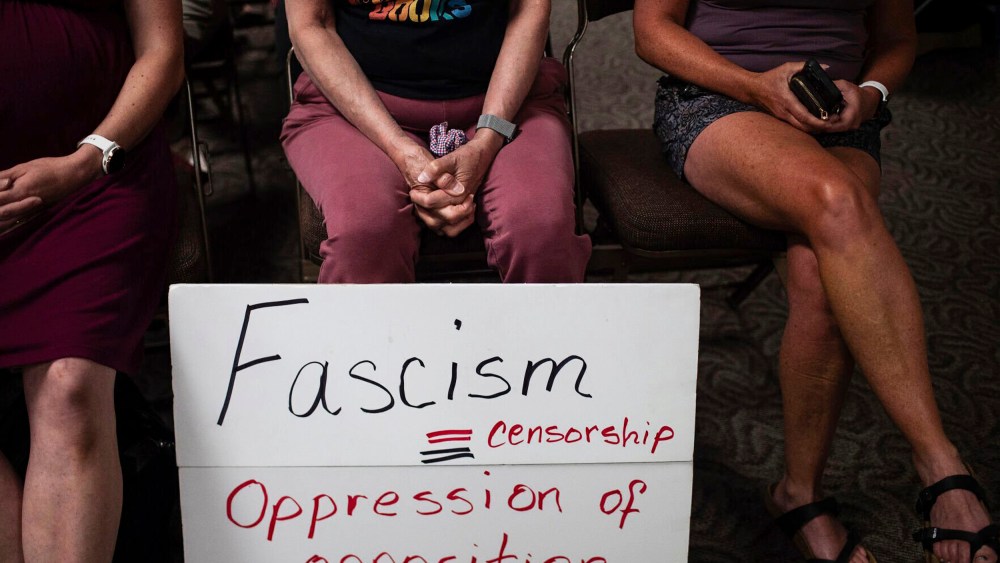 People sit with a sign at a Campbell County Library Board meeting