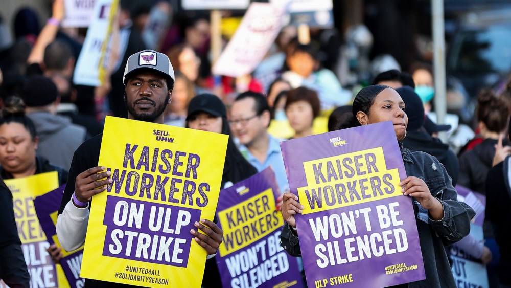 Striking Kaiser Permanente workers hold signs in front of the Kaiser Permanente San Francisco Medical Center.