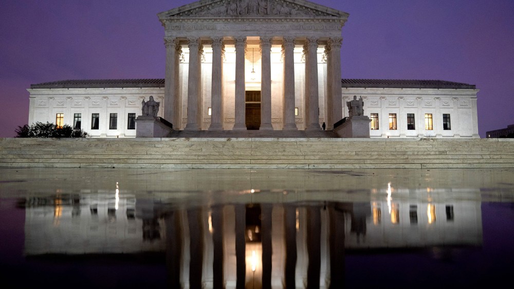 The US Supreme Court is reflected in a puddle of water at night.