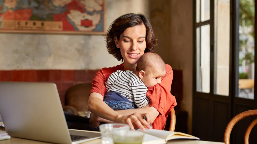 Mother carrying baby while reading book at table
