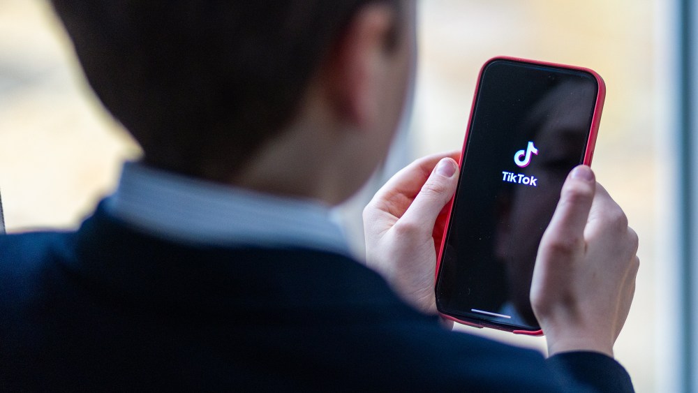 Boy looks at an iPhone screen showing TikTok logo
