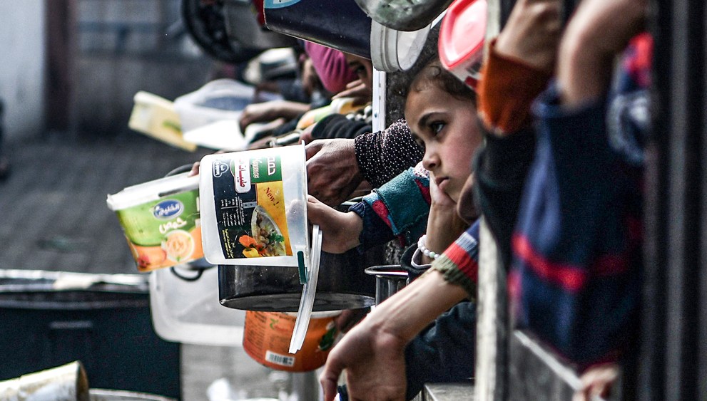 Palestinians hold out their empty containers to be filled with food behind bars.