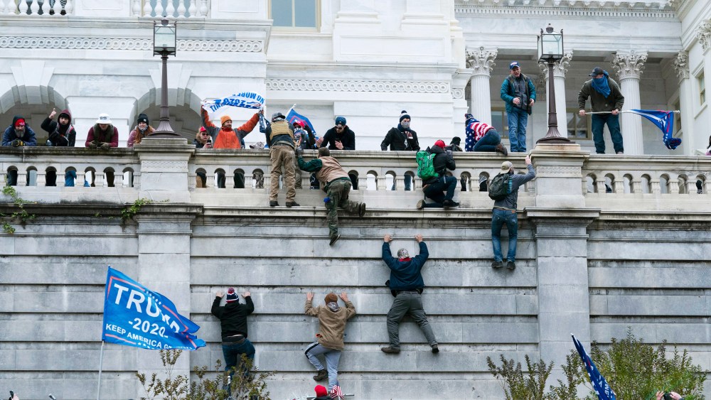 Rioters climb the west wall of the the Capitol