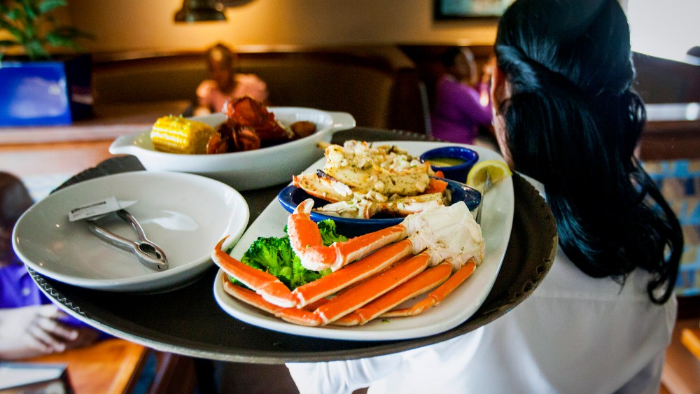 A waitress carries a tray a lobster kettle and a crab trio dish at a Red Lobster restaurant.