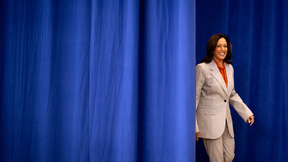 Kamala Harris walks through a blue curtain