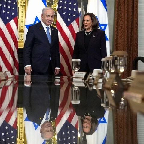 Benjamin Netanyahu and Kamala Harris stand next to each other in a conference room, their reflections are seen on the table in front of them