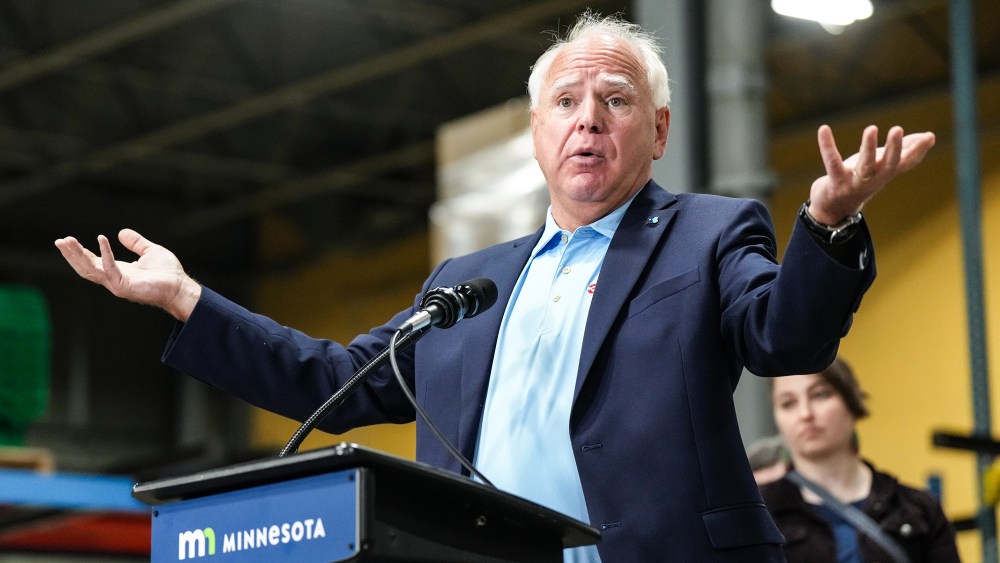 Tim Walz speaks at a podium, raises his hands
