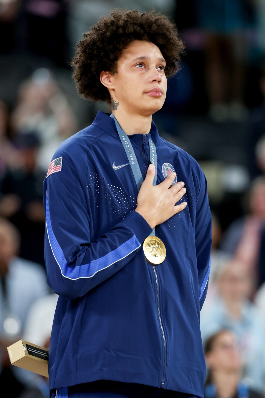 Brittney Griner is teary eyed with her hand on her chest, wearing her olympic gold medal