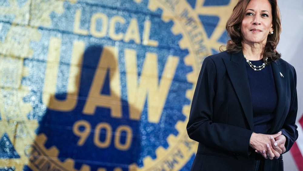 Kamala Harris stands in front of a wall painted with the UAW logo