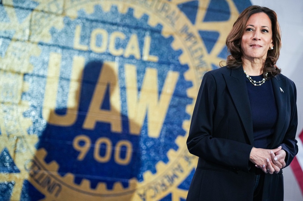 Kamala Harris stands in front of a wall painted with the UAW logo