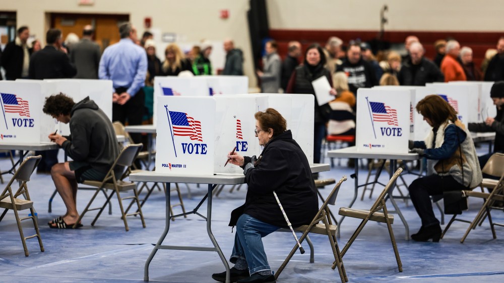 Voters fill out their ballots at a polling location behind dividers that say "Vote" with the American flag