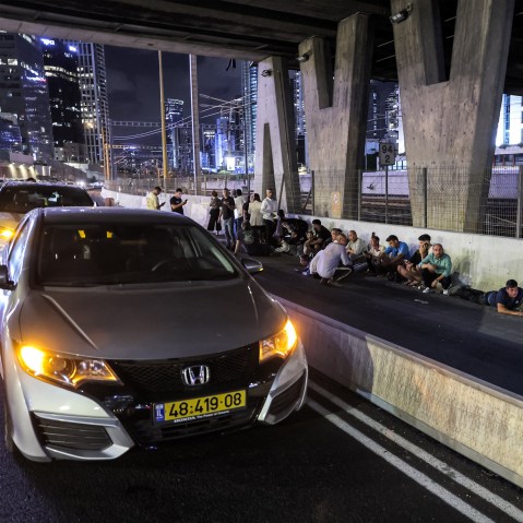 People take cover behind vehicles under a bridge in Tel Aviv