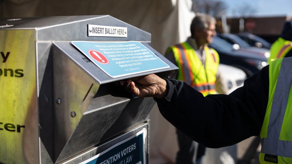 An election worker places a ballot in a drop-off box