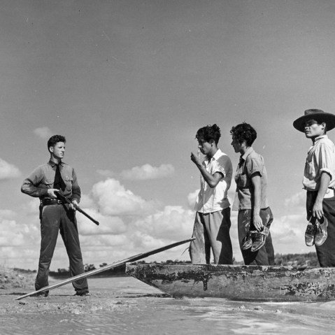 Two armed American border guards deter a group of immigrants.