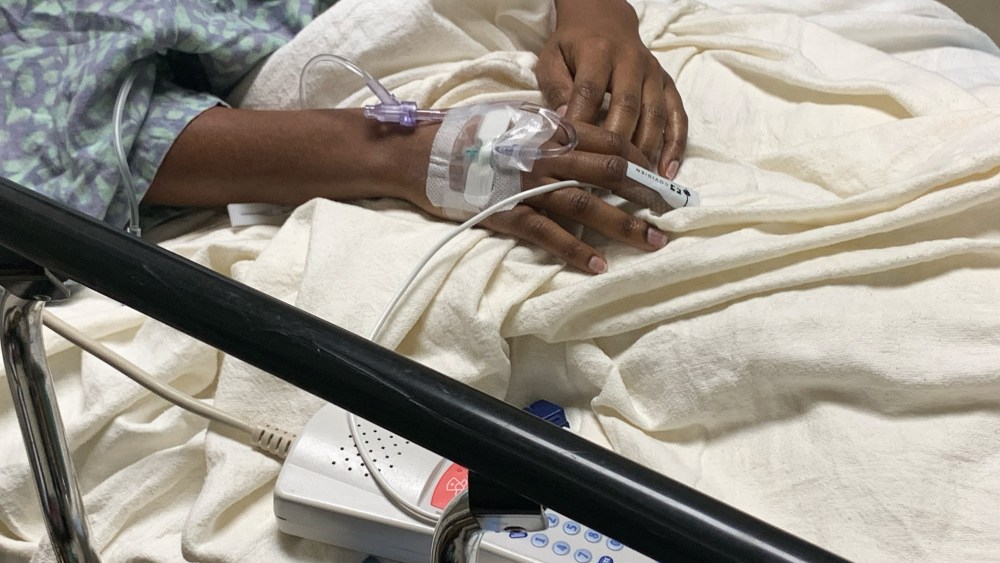 Hands connected to tubes are seen on a hospital bed
