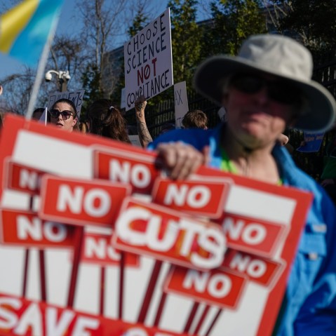 A person holds a "No no no no cuts" sign outside the CDC during a protest.
