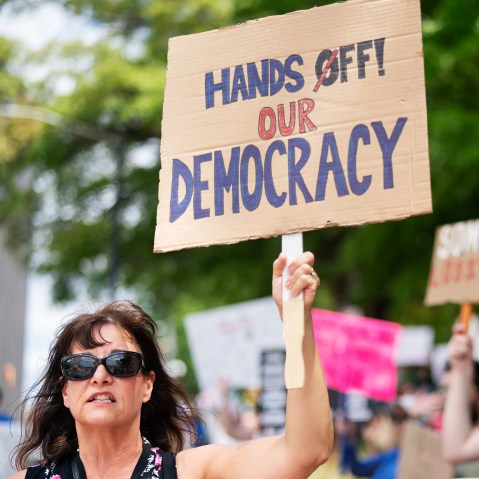 A protester holds a sign that reads, "Hands Off Our Democracy"