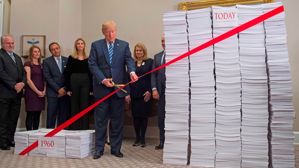 President Donald Trump uses gold scissors to cut red tape between  stacks of papers representing government regulations on Dec. 14, 2017, at the White House.