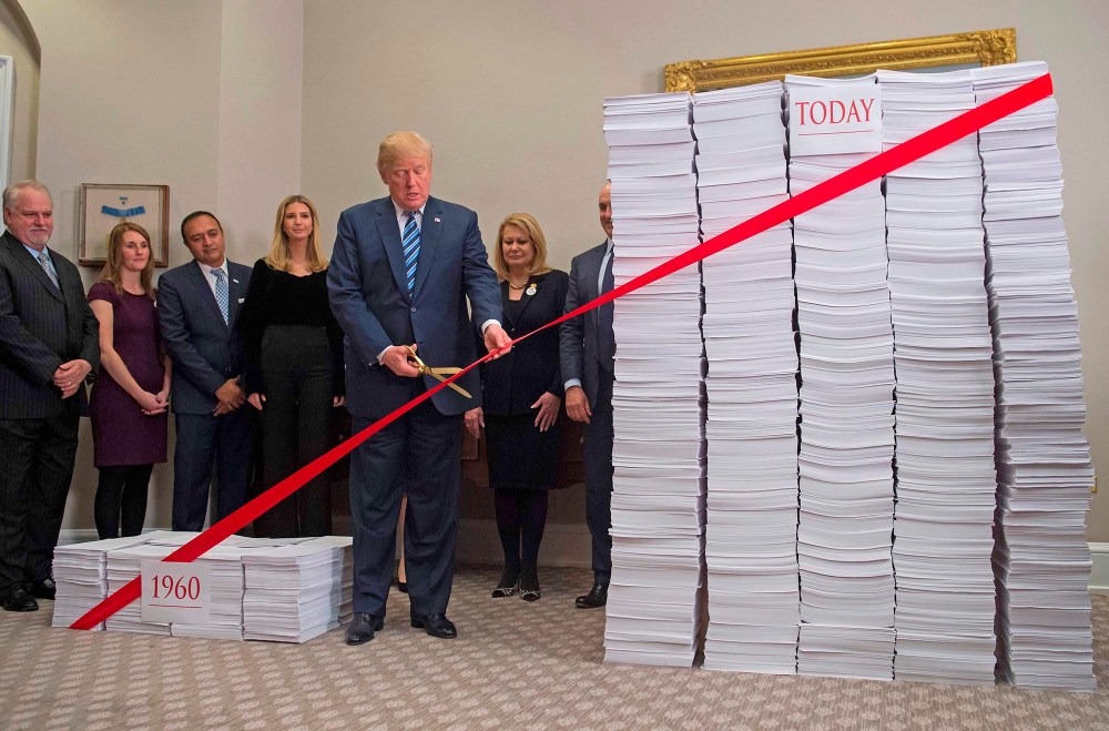 President Donald Trump uses gold scissors to cut red tape between stacks of papers representing government regulations on Dec. 14, 2017, at the White House.