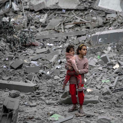 A Palestinian girl carries a child through the rubble of houses destroyed by Israeli bombardment in Gaza City