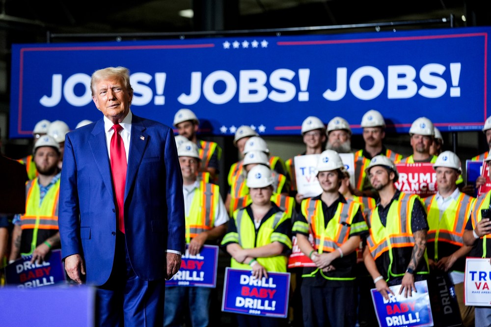 Donald Trump stands on stage in front of workers wearing safety vests