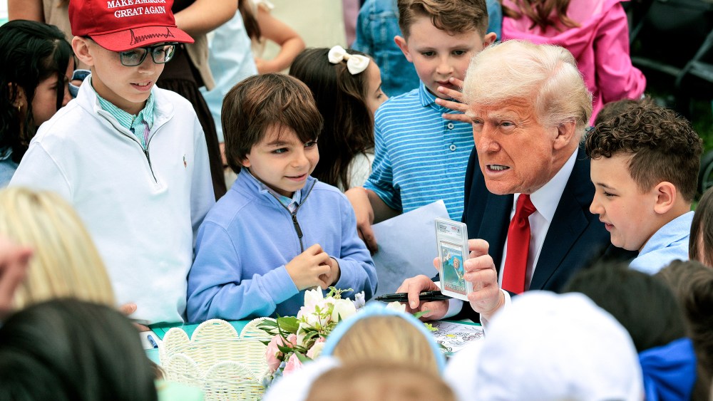 President Donald Trump shows a group of children a trading card of himself while sitting outside