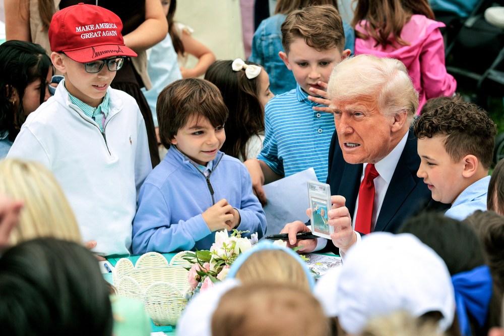 President Donald Trump shows a group of children a trading card of himself while sitting outside