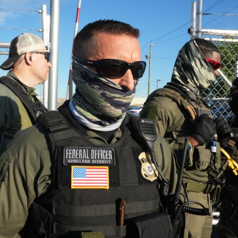 Immigration and Customs Enforcement agents stand near a gate, wearing face covering