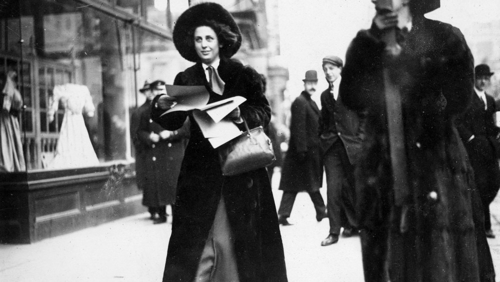 Miss Martha Gruening distributes literature publicizing the Women's Suffrage Movement to passers-by outside the Lyceum Theatre, circa 1912.