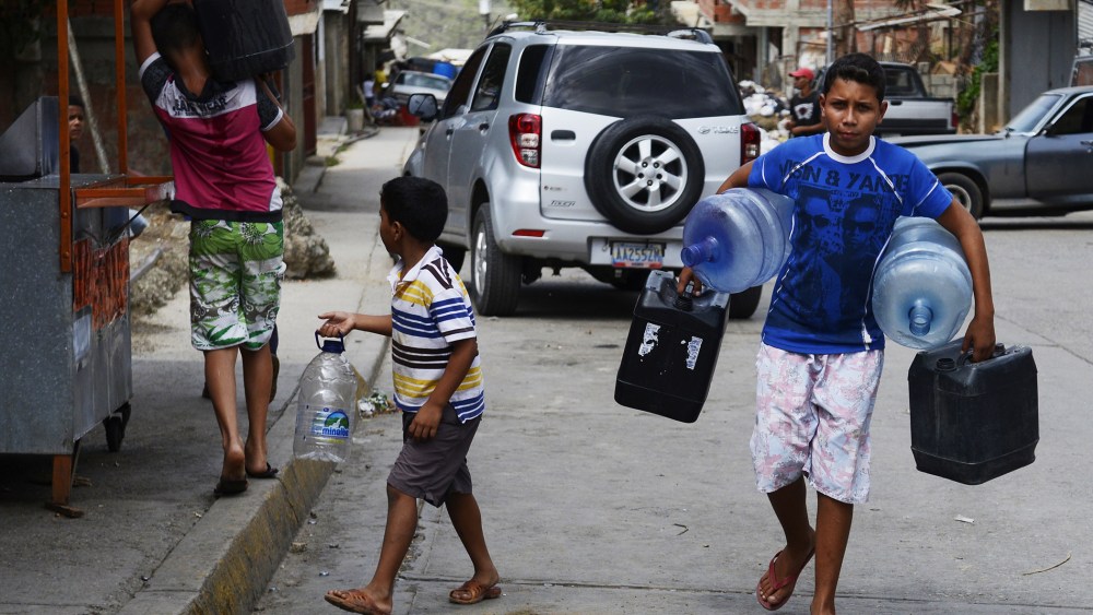 Boys carry empty bottles and cans to fill them with water in Caucaguita, Caracas, on June 20, 2014.