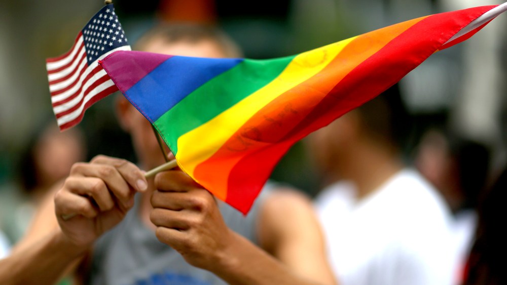 A protester holds an American flag and a rainbow flag.
