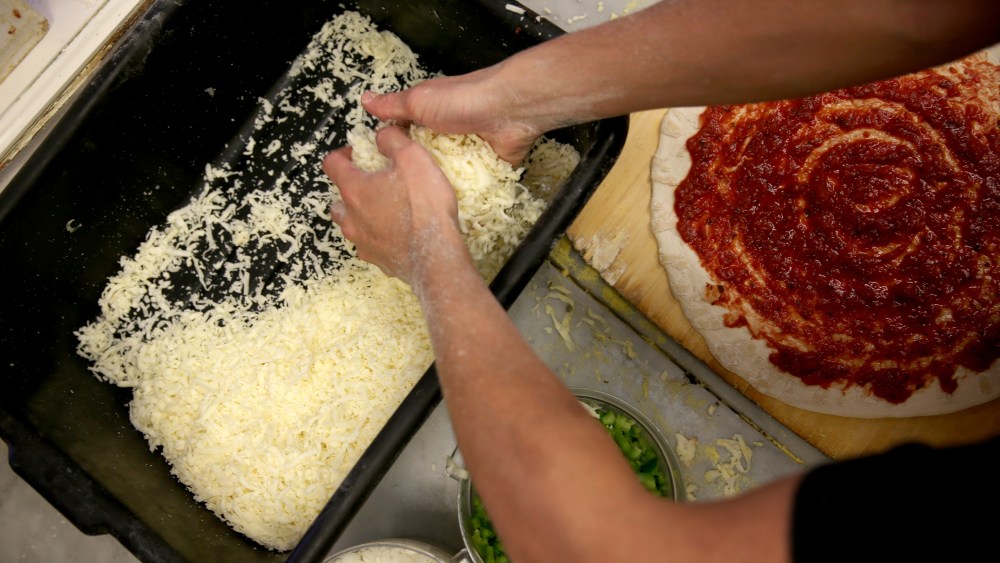 An employee spreads cheese on a pizza. (Photo by Joe Raedle/Getty)