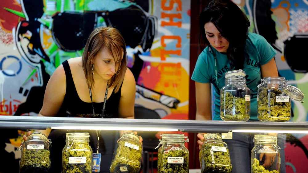 Brittany Zewe, left, and Jess Vanderpool take jars of different strains of marijuana off the counter between customers at Denver Kush Club in Denver, Colorado on Jan. 1, 2014.