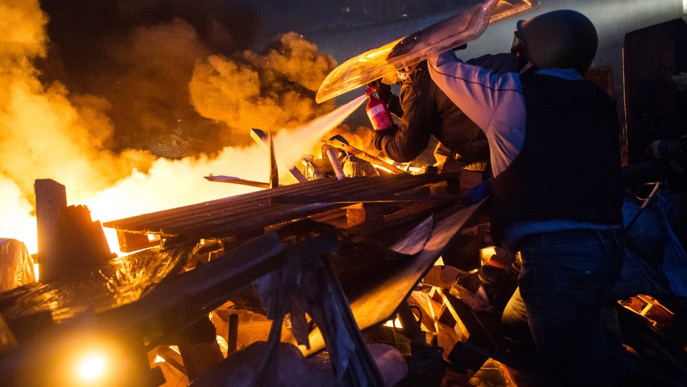 Anti-government protesters stand behing their burning barricades during clashes with police in the center of Kiev.