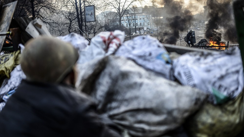 An anti-government protester looks at a protester adding tires to a fire at a barricade on February 21, 2014 in Kiev.