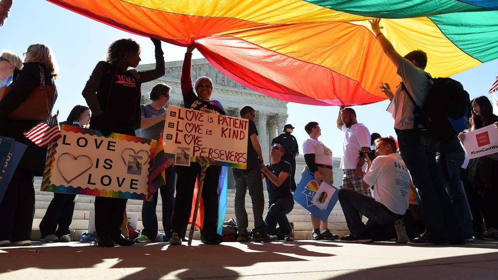 Supporters of gay marriage stand beneath a large rainbow flag which is placed in support of gay marriage in front of the U.S. Supreme Court in Washington, D.C., April 28, 2015. (Photo by Astrid Riecken/Washington Post/Getty)