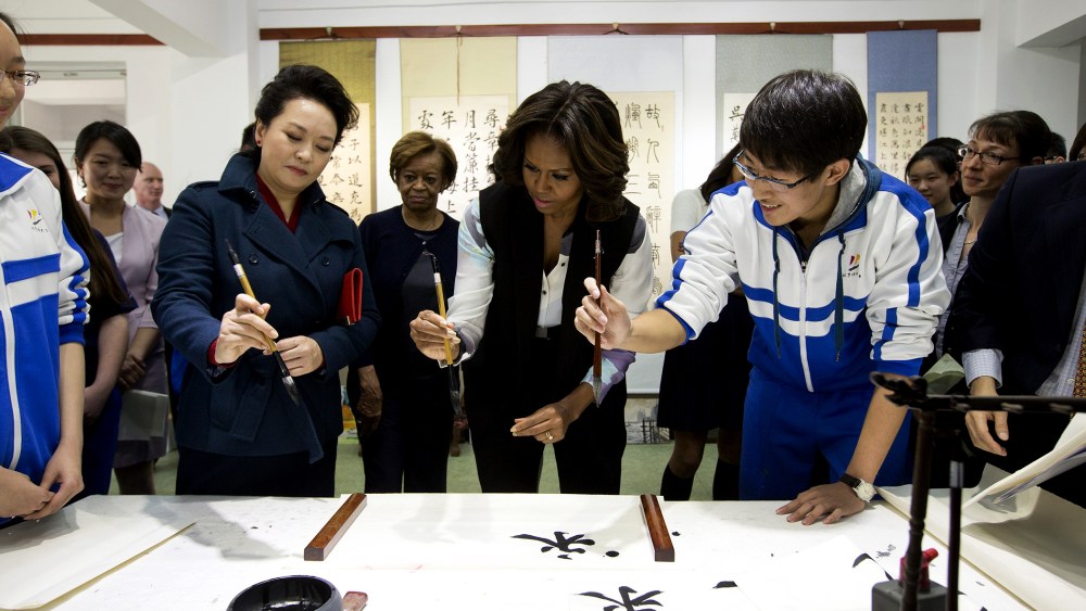 Peng Liyuan (L), wife of Chinese President Xi Jinping, shows First Lady Michelle Obama how to hold a writing brush as they visit a Chinese traditional calligraphy class at the Beijing Normal School, March 21, 2014 in Beijing, China.