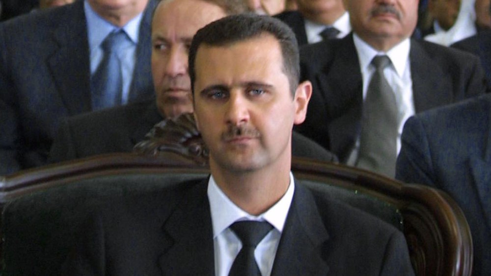 File Photo: Syrian President Bashar al-Assad (C) attends a ceremony marking the one-year anniversary his father's death in the northern city of Qerdaha 10 June 2001. (Photo by Louai Beshara/AFP/Getty Images File)