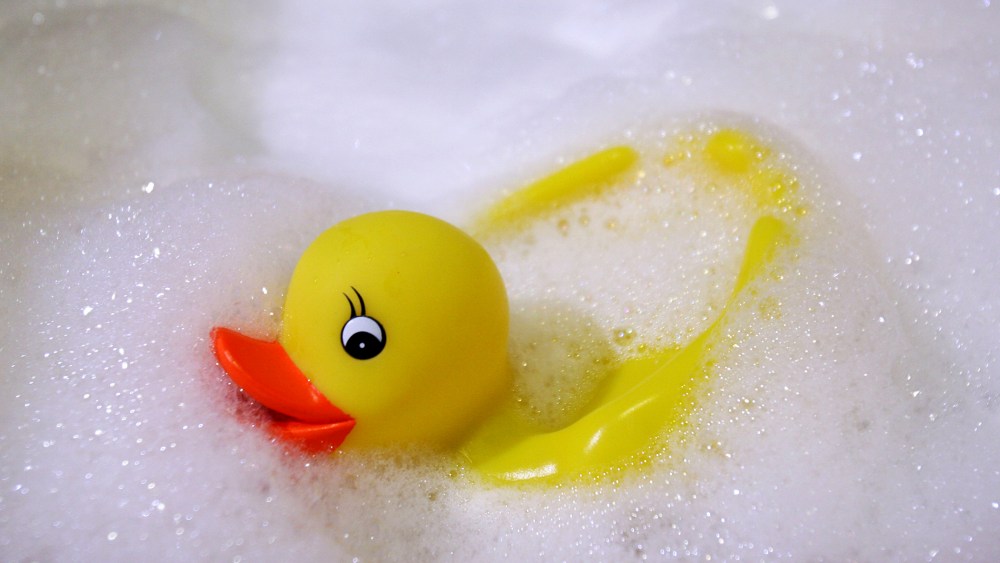 A rubber duck swims in a foam bath in a bath tub.