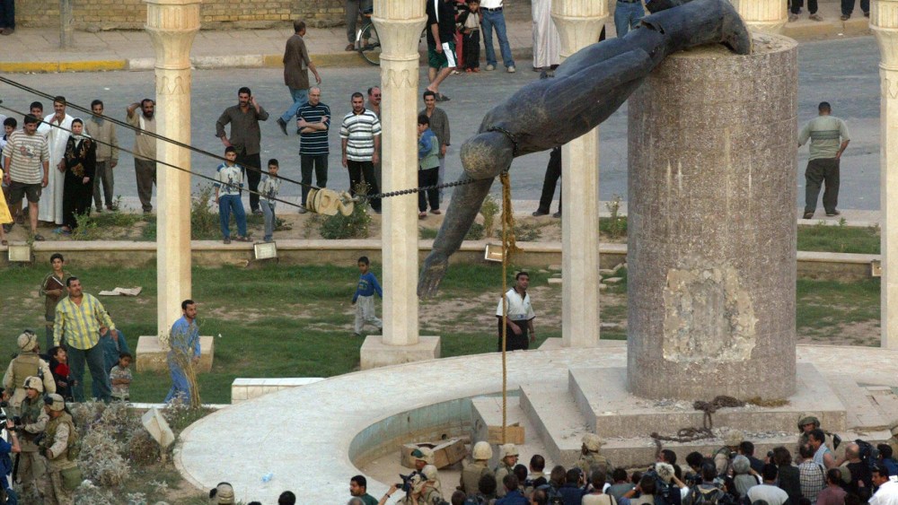 Iraqis watching a statue of Iraqi President Saddam Hussein as it is pulled down in Baghdad's al-Fardous square on April 9, 2003. (Photo by Patrick Baz/AFP/Getty Images, File)