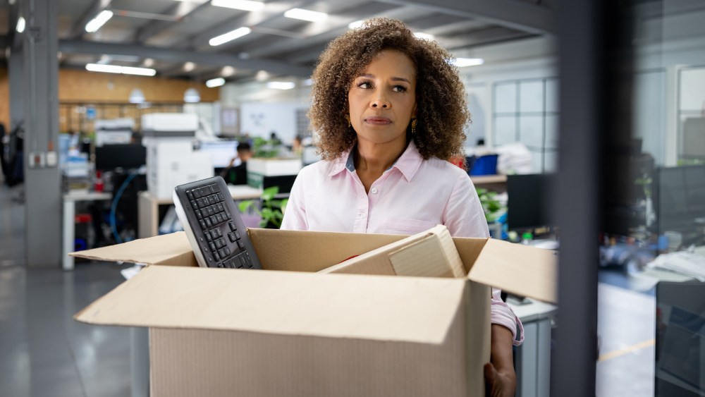 Business woman being fired from her office and carrying a box with her belongings