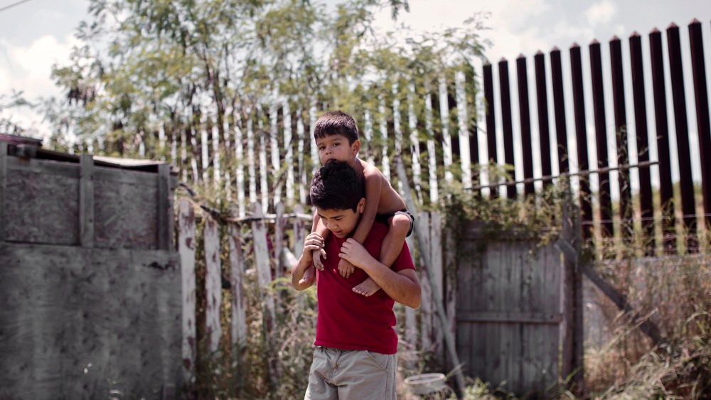 Damian Juarez, a boy whose backyard is lined by the border fence, plays with his little brother in Brownsville, Texas. (Photo by Bryan Schutmaat for MSNBC)
